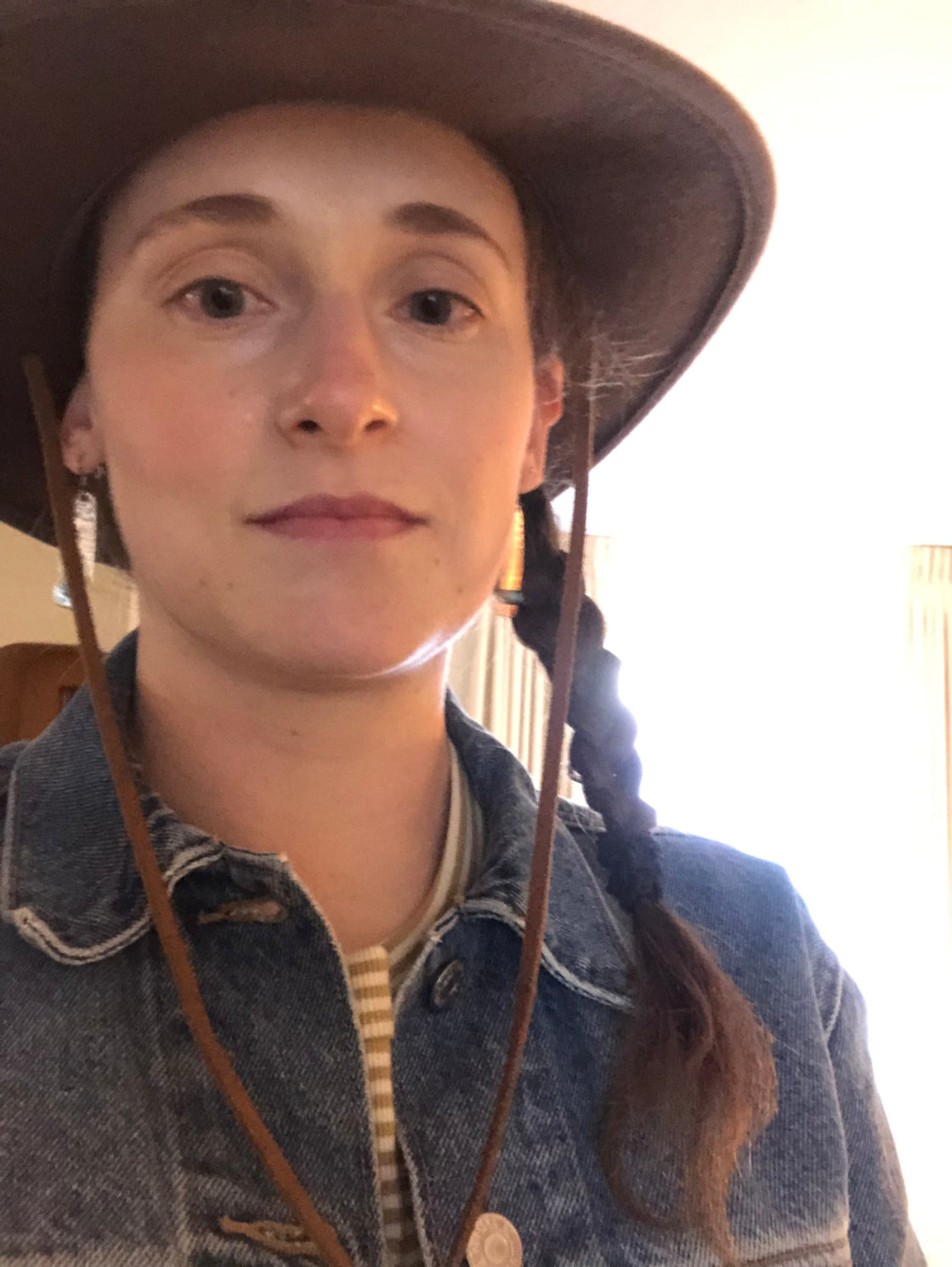 Person wearing a wide-brimmed hat and denim jacket indoors