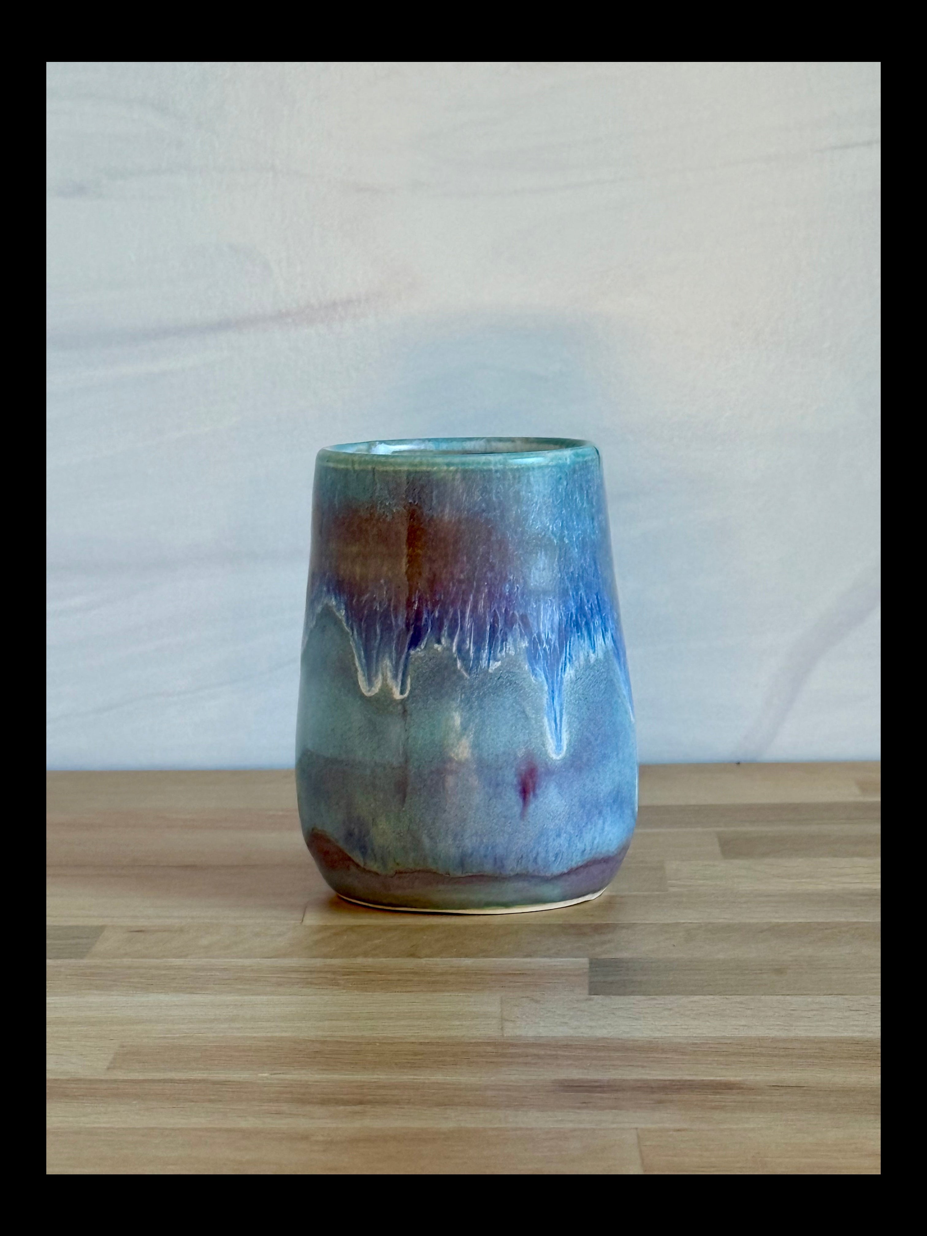 Ceramic tumbler with a multicolored glaze on a wooden surface.